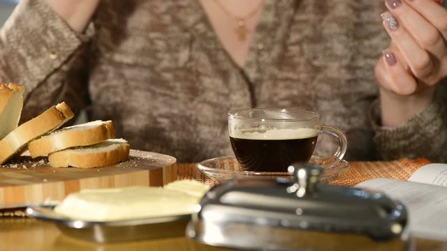 The woman with fine manicure has black coffee and eats sandwich from white loaf with butter