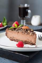 Slice of chocolate cheesecake decorated with nuts, raspberries and mint leaf. Closeup view, vertical composition