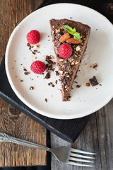 Slice of chocolate cheesecake decorated with raspberries, nuts and mint leaf on white plate. Table top view, vertical composition