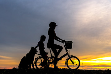 Fototapeta na wymiar Silhouette biker lovely family at sunset over the ocean. Mom and daughter with dog bicycling at the beach. Lifestyle Concept.