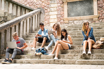 Teenage students with gadgets outside on stone steps.
