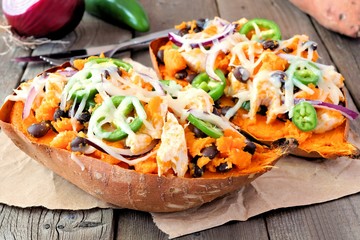 Baked sweet potatoes stuffed with chicken, vegetables and cheese, close up on a rustic wood...