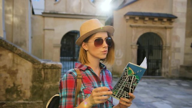 Beautiful young woman in stylish hat using paper map while traveling in the beatiful old city.