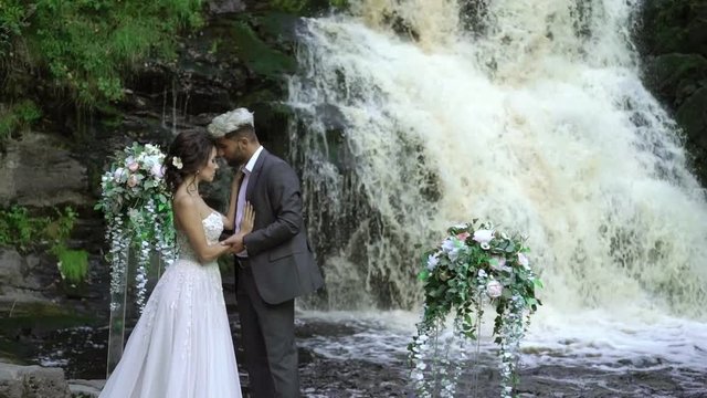 Young wedding couple staying at ceremony near waterfall