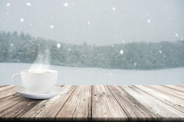 Cup of coffee on wooden table with winter snowfall covered forest. Vintage color tone and rustic style.