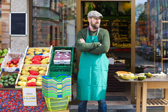 Grocer with arms crossed in front of greengrocer's shop