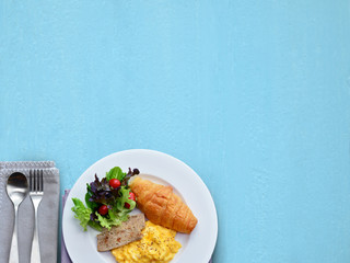 Breakfast set ( Scrambled egg, croissant and vietnamese pork sausage with black pepper) on left corner and blue background. Copy space