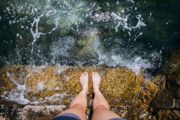 View from top of camera of person making photos of legs standing on pier or step and waves rolling over, beautiful crystal clear water