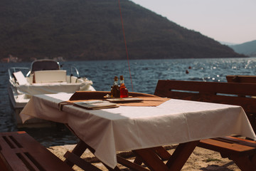 Beautiful arranged table for dinner or lunch near adriatic sea, overlooking kotor bay in montenegro with white sheets and extra virgin olive oil, unfocused yacht in background