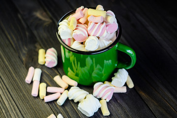 The green enameled mug is filled with a multicolored marshmallow on a black wooden table top view