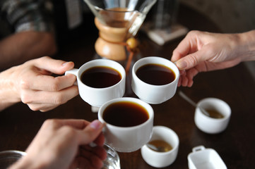 Clink glasses with three cups of coffee on the background of coffee items at the tasting