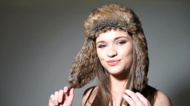 Closeup portrait of pretty young brunette woman in fur hat with her hands to the ear flaps smiling at the camera