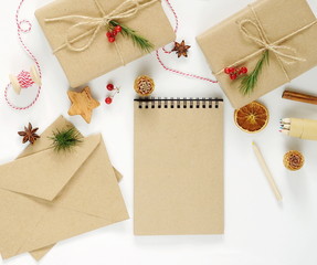 Christmas composition with decorations , gifts packed in craft paper, notepad for text and postal envelopes on white background.Top view. Flat lay. Copy space