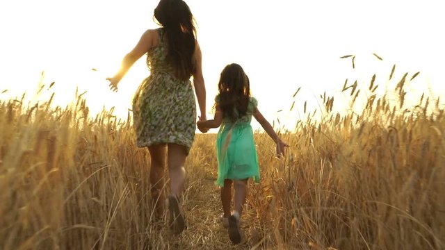 young mom with girl in the dress is running across the field.