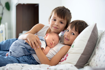 Two children, toddler and his big brother, hugging and kissing their newborn baby brother