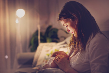 Young beautiful mother, breastfeeding her newborn baby boy at night