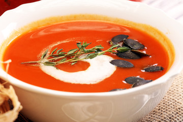 Roasted pumpkin and carrot soup with cream and pumpkin seeds on wooden background.