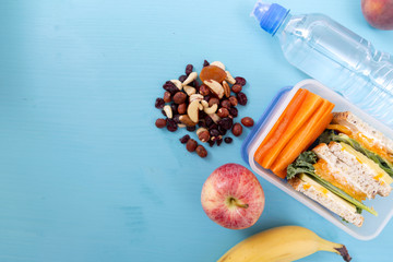 School lunch box with sandwich, vegetables, water, nuts and fruits on turquoise background. Healthy eating habits concept