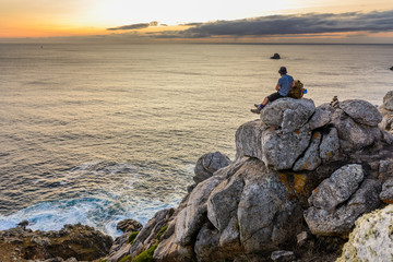 Fototapeta na wymiar tourist with a backpack sits on a rock looking at the sunset over the ocean