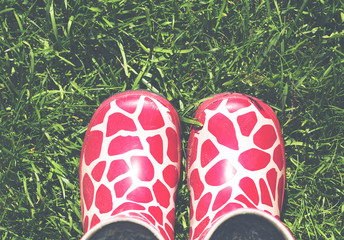 Small rubber boots on the green grass. Image has a vintage effect applied. Copy space.