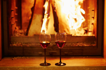 Two glasses of red wine near fireplace