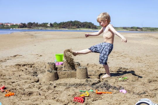 Boy kicking against sandcastle on beach