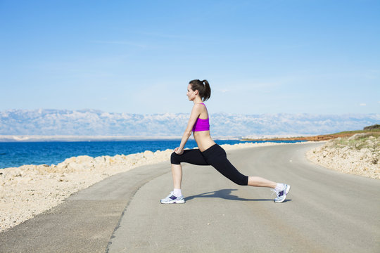Young woman stretching leg on waterfront path