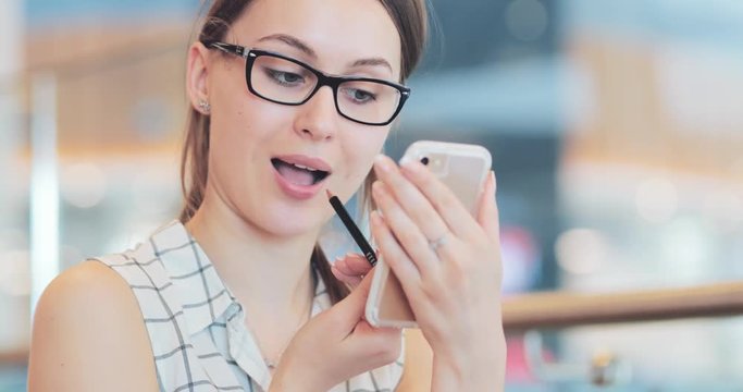 Young Woman Paint Her Lips, using Smartphone as Mirror. 4K DCi SLOW MOTION, CLOSE UP. Stylish Girl using lipstick in the shopping mall. Cinematic Shot