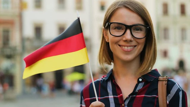 Caucasian woman in casual shirt with german flag posing on camera and smiling on the city street background.