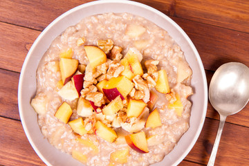 Porridge with peach, apple, banana and walnut on a wooden table