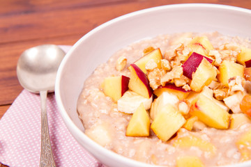 Porridge with peach, apple, banana and walnut on a wooden table