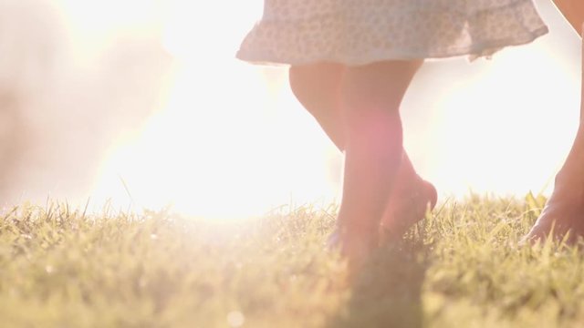 Little baby learns to walk. First Steps. Slow Motion 120 fps, 4K. Mother is teaching her child to do the first steps on a green grass in summer. Close up on feet. Happy childhood and Maternity. Family