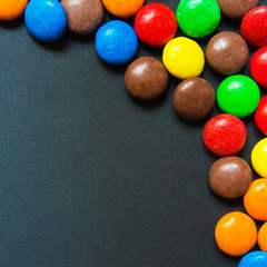 Multicolored sweets in the form of a dragee on a dark background pattern frame background