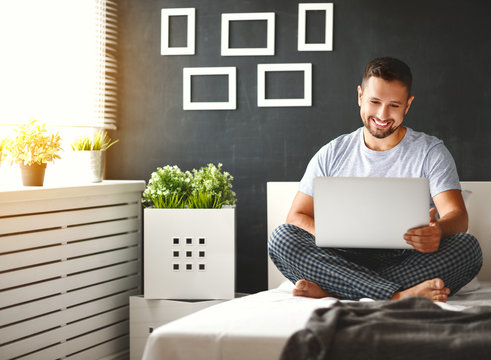 happy young man with laptop in bed