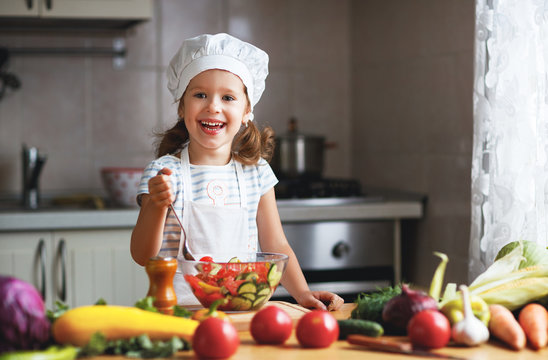 Healthy eating. Happy child girl prepares  vegetable salad in kitchen