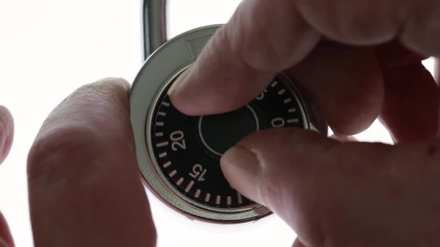 Very close video of unlocking a combination padlock atop a white background..