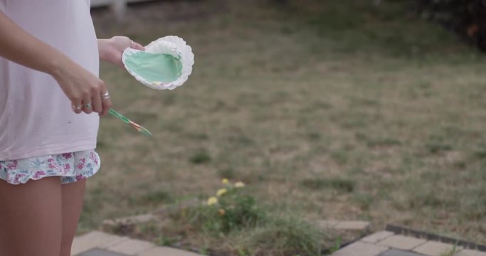 Woman paints abstract painting in yard - close up paint brush