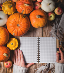 Hands on the notebook and autumn composition with pumpkins on wood background