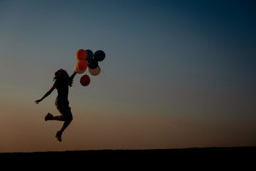 silhouette of young woman with flying balloons against the sky.
