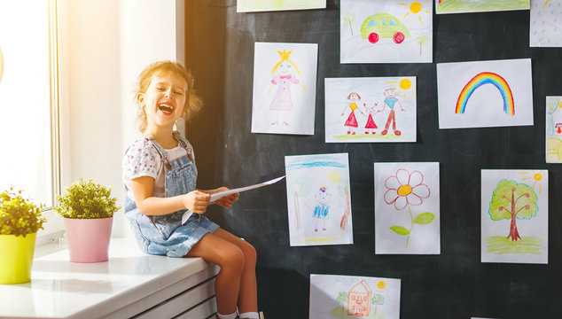 child girl hanging her drawings on wall