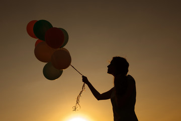 silhouette of young woman with flying balloons against the sky.