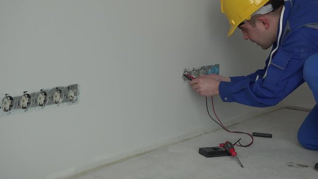 Professional male electrician using special tool to check wall socket voltage