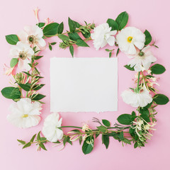 Frame made of flowers with leaves and white card on pink background. Flat lay, top view. Flower background.