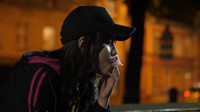 An angry sad teen girl with a cigarette. Night in park.