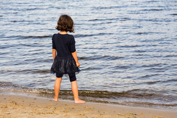 Girl in blue dress at the beach looking at the sea