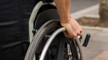 Obraz premium Close-up of male hand on wheel of wheelchair during walk in park