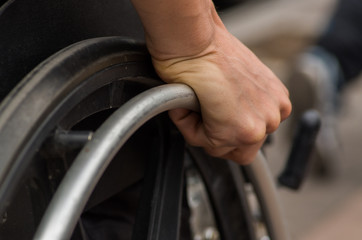 Close-up of male hand on wheel of wheelchair during walk in park