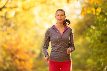Young brunette woman running in autumn forest listening to mps music