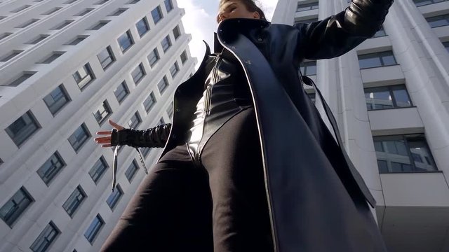 slow motion. 500 frames per second. stylish young girl in leather long coat. shot from the bottom of a larger plan. background large white building