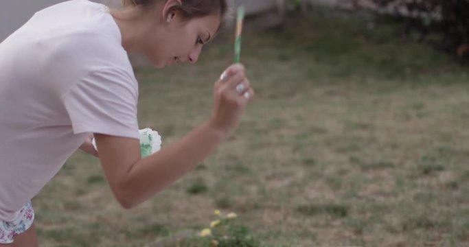 Woman paints abstract painting in yard - close up on face